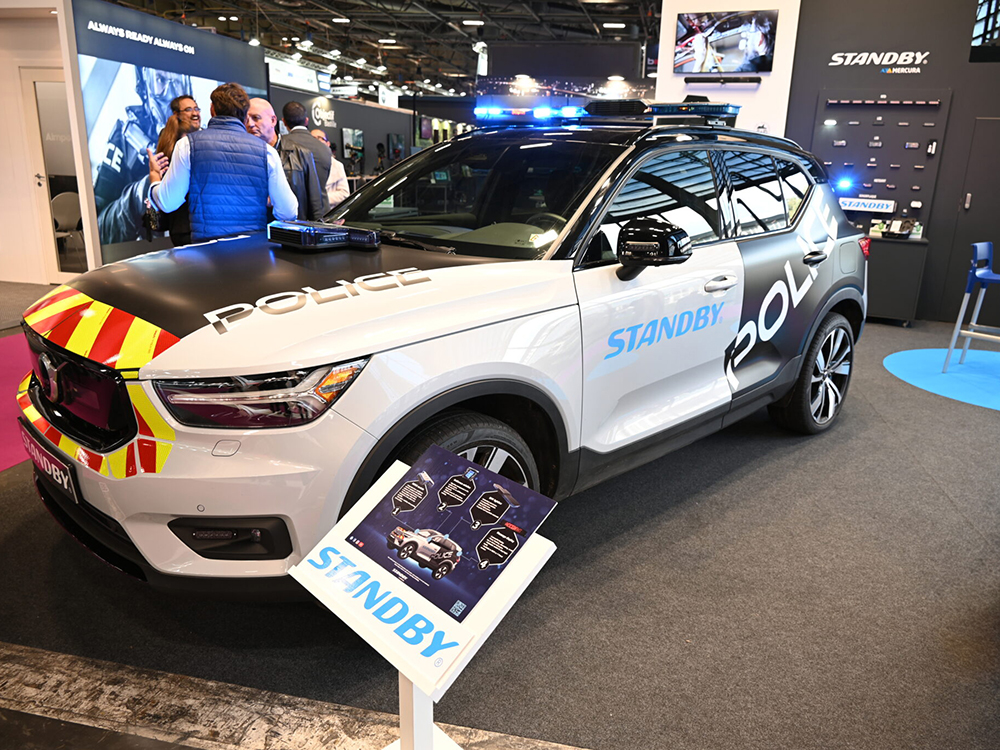 Close up shot of the Standby Mercura stand with an angle view of a car on the lefthand side and products on wall in background. People stand behind the car talking.