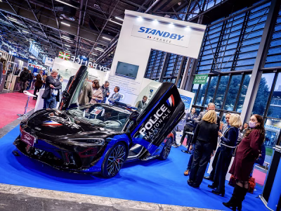 Angled view of the Standby France / Standby Group stand at Milipol Paris 2025. A black McLaren with Police Nationale livery is parked on the stand at an angle with open upward-opening doors. Groups of people are dotted around the stand.