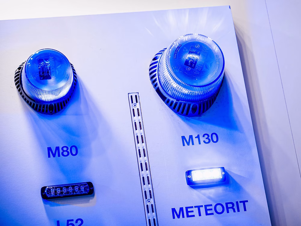 Closely cropped angle view of the M80 & M130 beacons and L52 and Meteorit LED Modules on a white panel on the Standby France / Standby Group stand at Milipol Paris 2025. The L52 is the only one unlit.