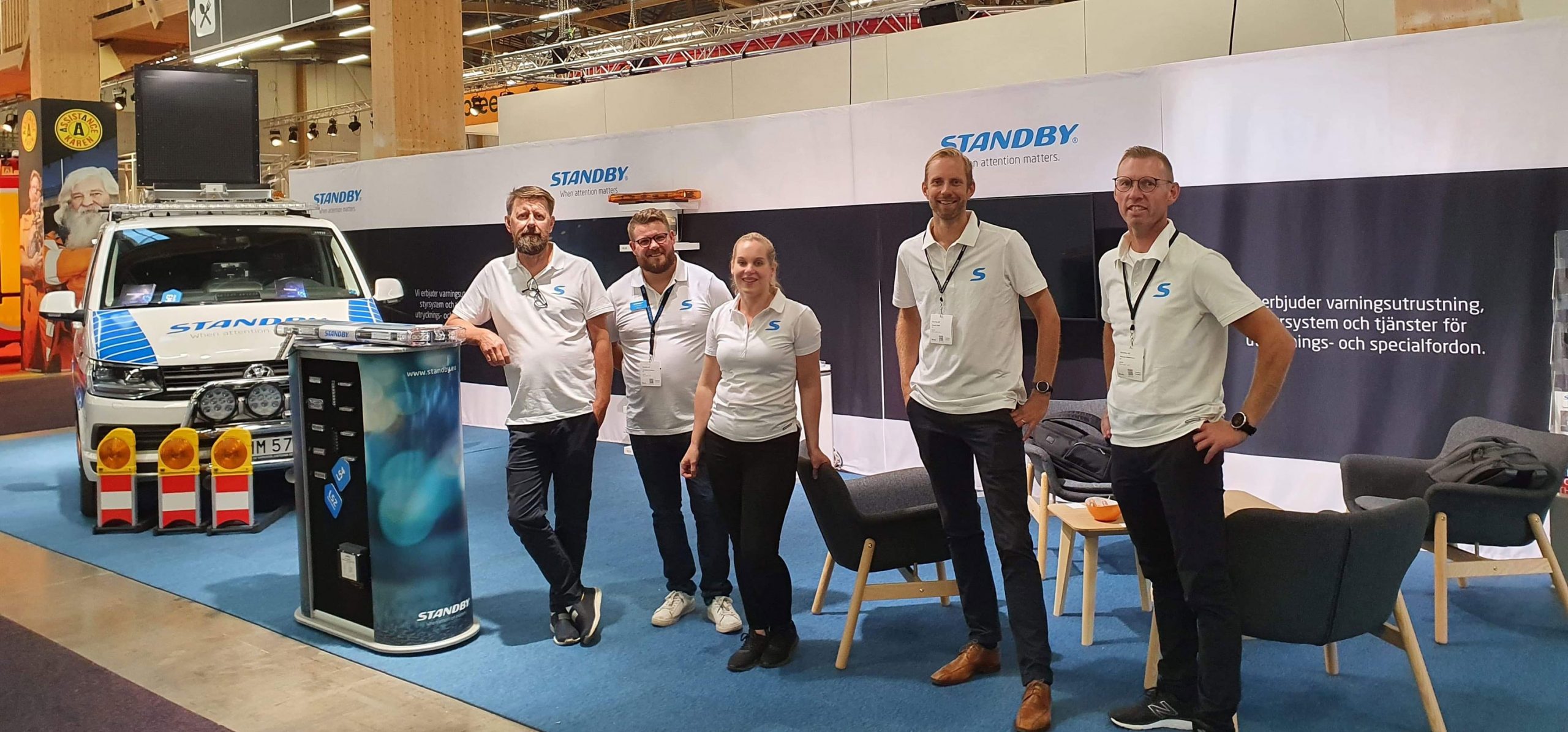 Standby medarbetare med vita skjortor står på rad i en mässmonter.