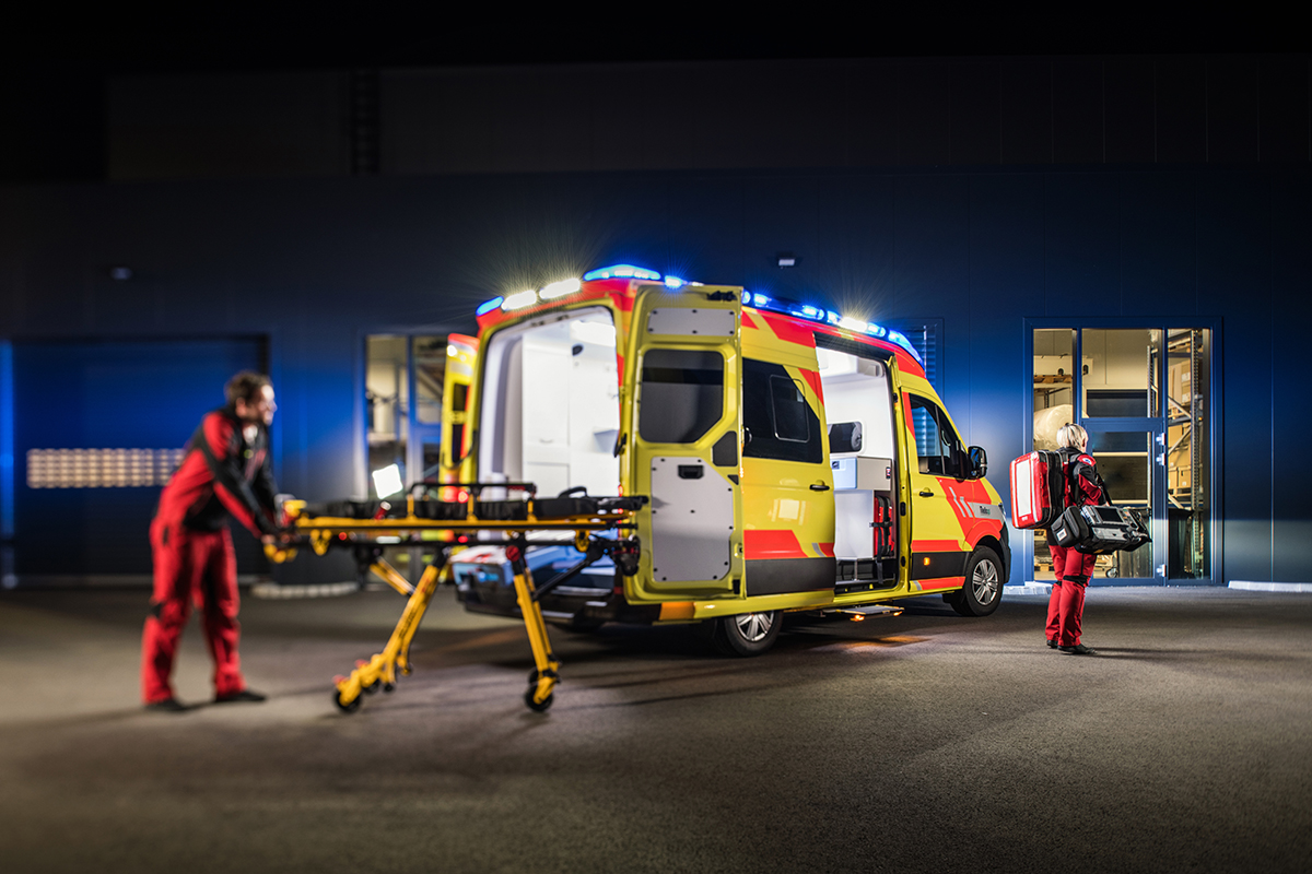 En ambulans bakifrån på sidan i mörker med två sjukvårdare som kör en bår.