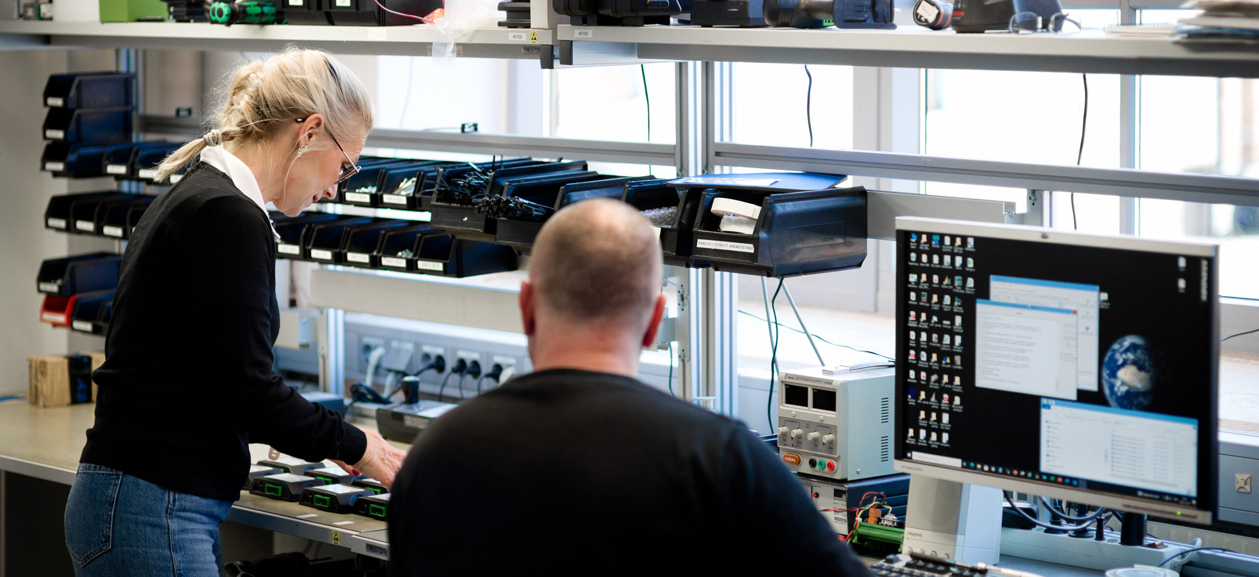 Två medarbetare som arbetar vid en arbetsbänk med en dator bredvid.