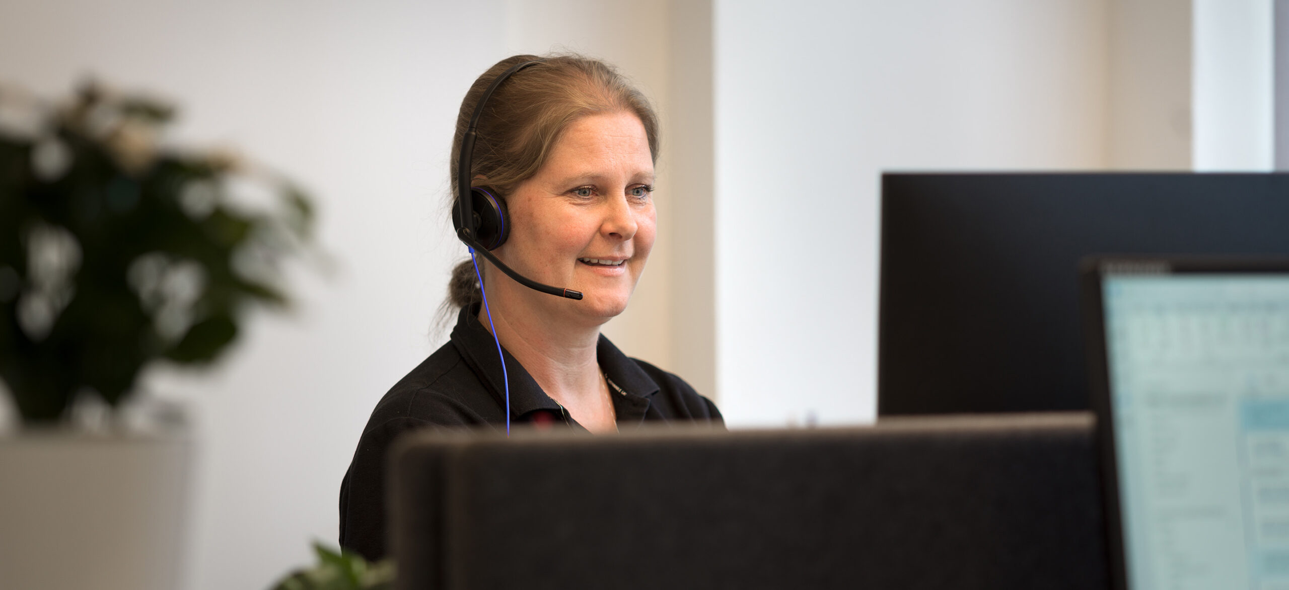 En medarbetare jobbar vid en dator med ett headset på huvudet.