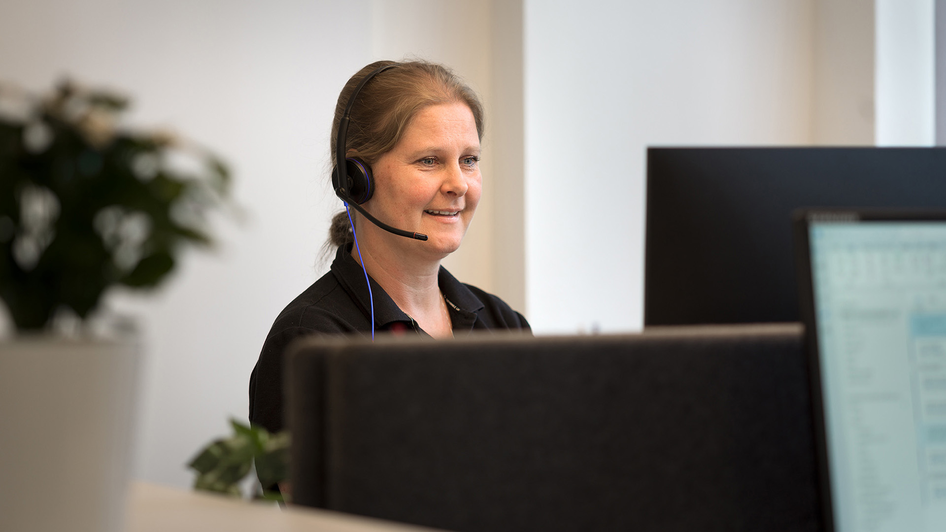 Glad medarbetare med headset sitter vid dator.