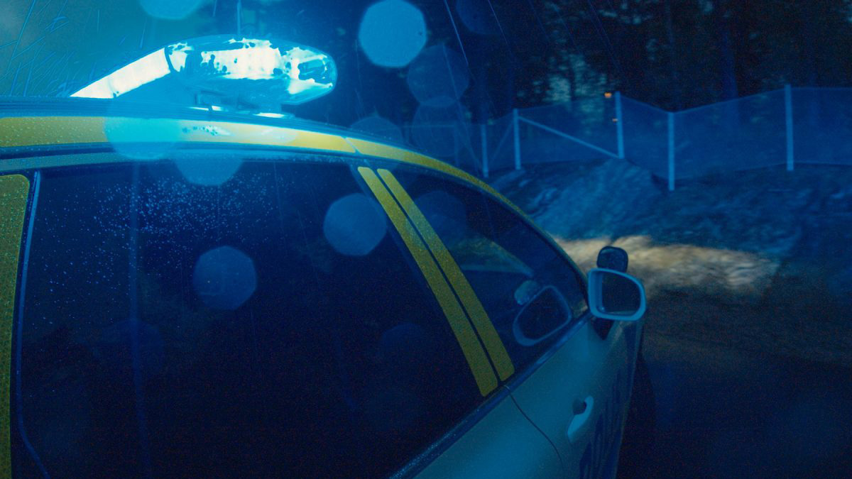 Polisbil med ljusramp lyser upp i mörker vid ett staket.