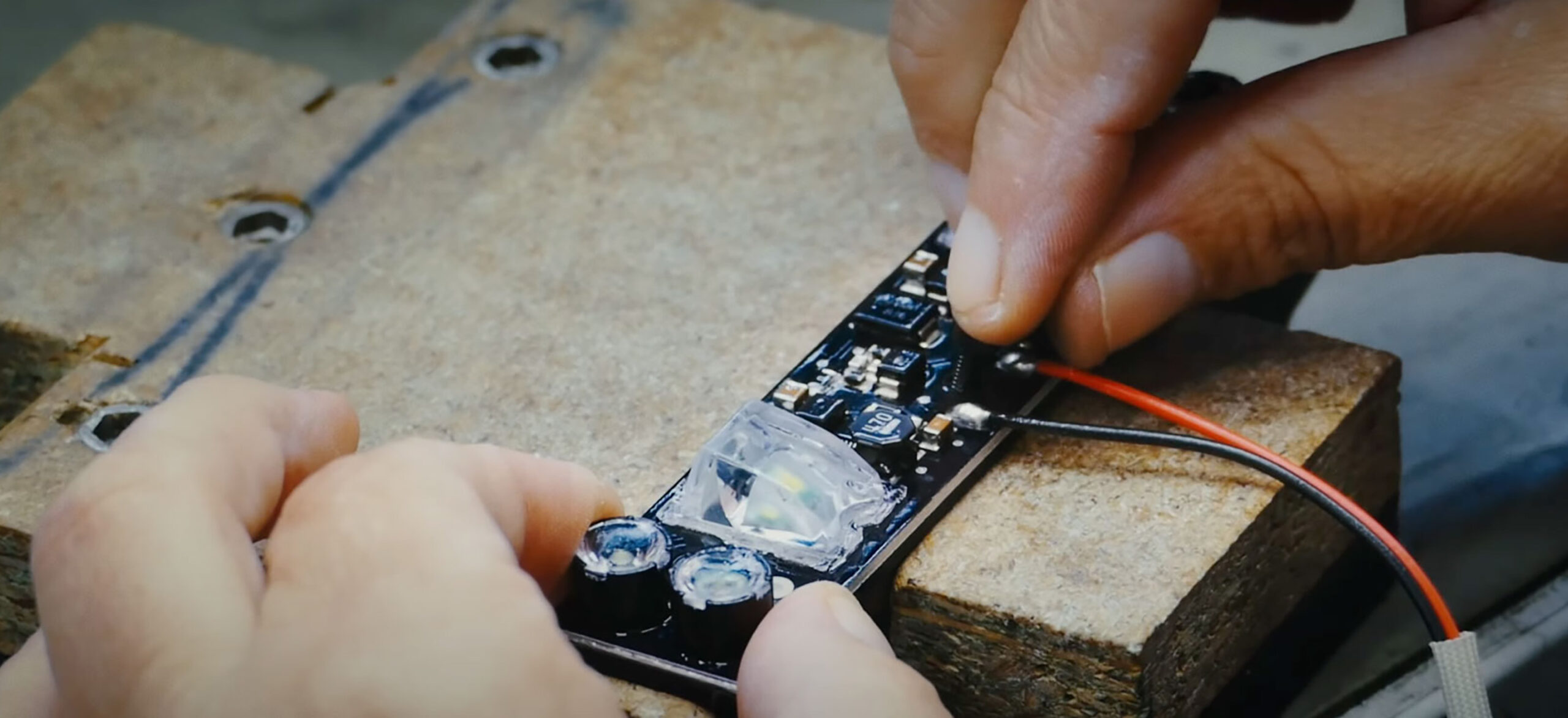 Närbild på två händer som arbetar med ett kretskort på en arbetsbänk.