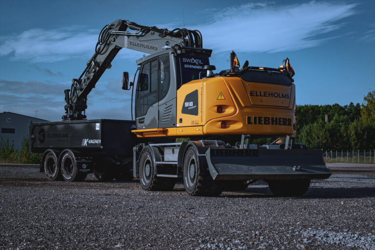 En grävmaskin fyller upp sin släpvagn med grus.