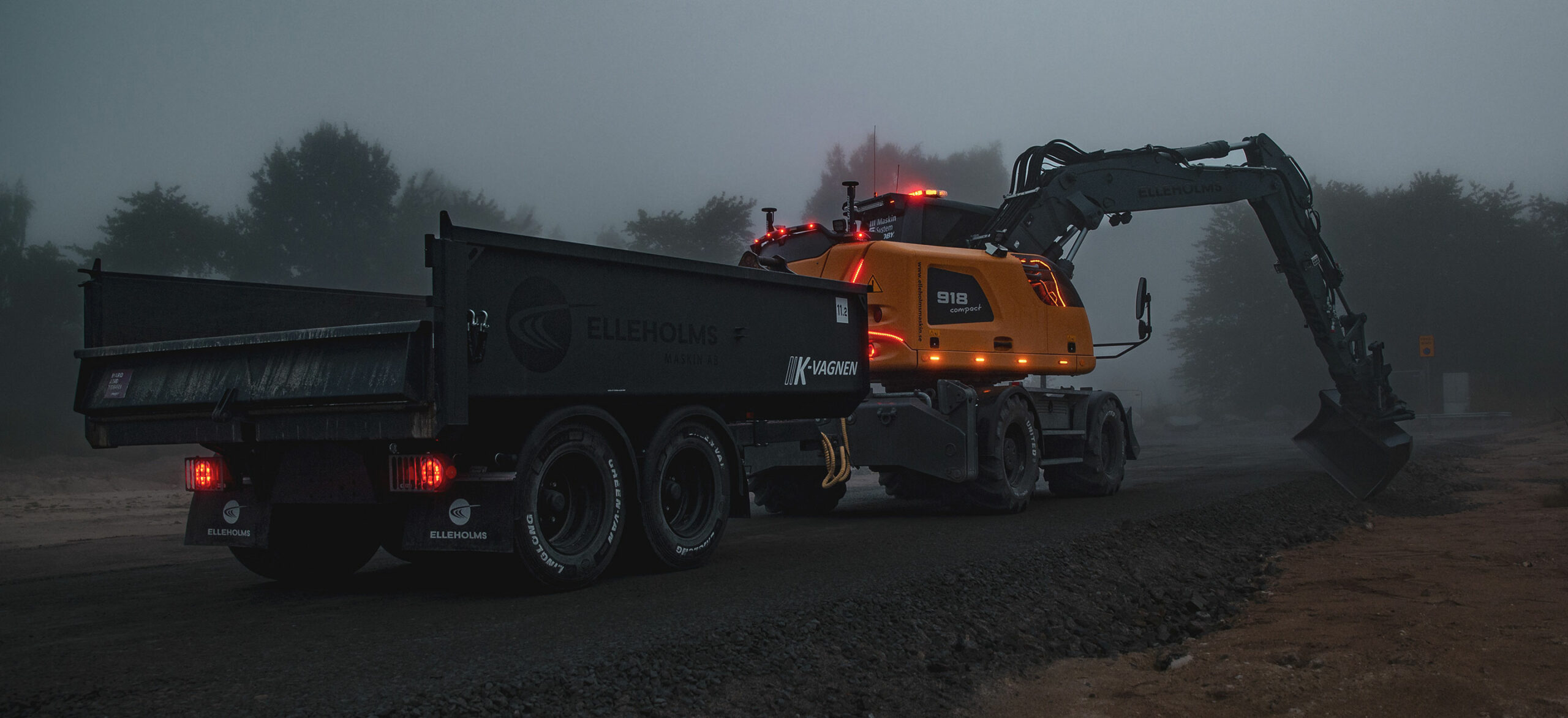 En grävmaskin med släåvagn gräver i ett grustag i dimmigt gryningsljus.