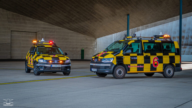 Två styckern flygplatsfordon parkerade under tak.