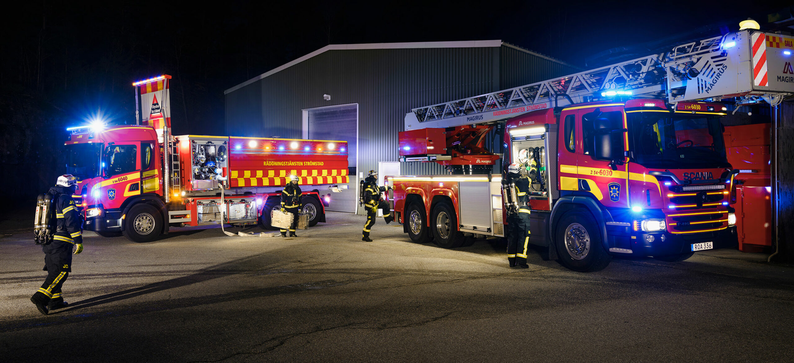 Två brandbilar står utanför en lokal i mörker med blåljus på och personal vid sidan av bilarna.