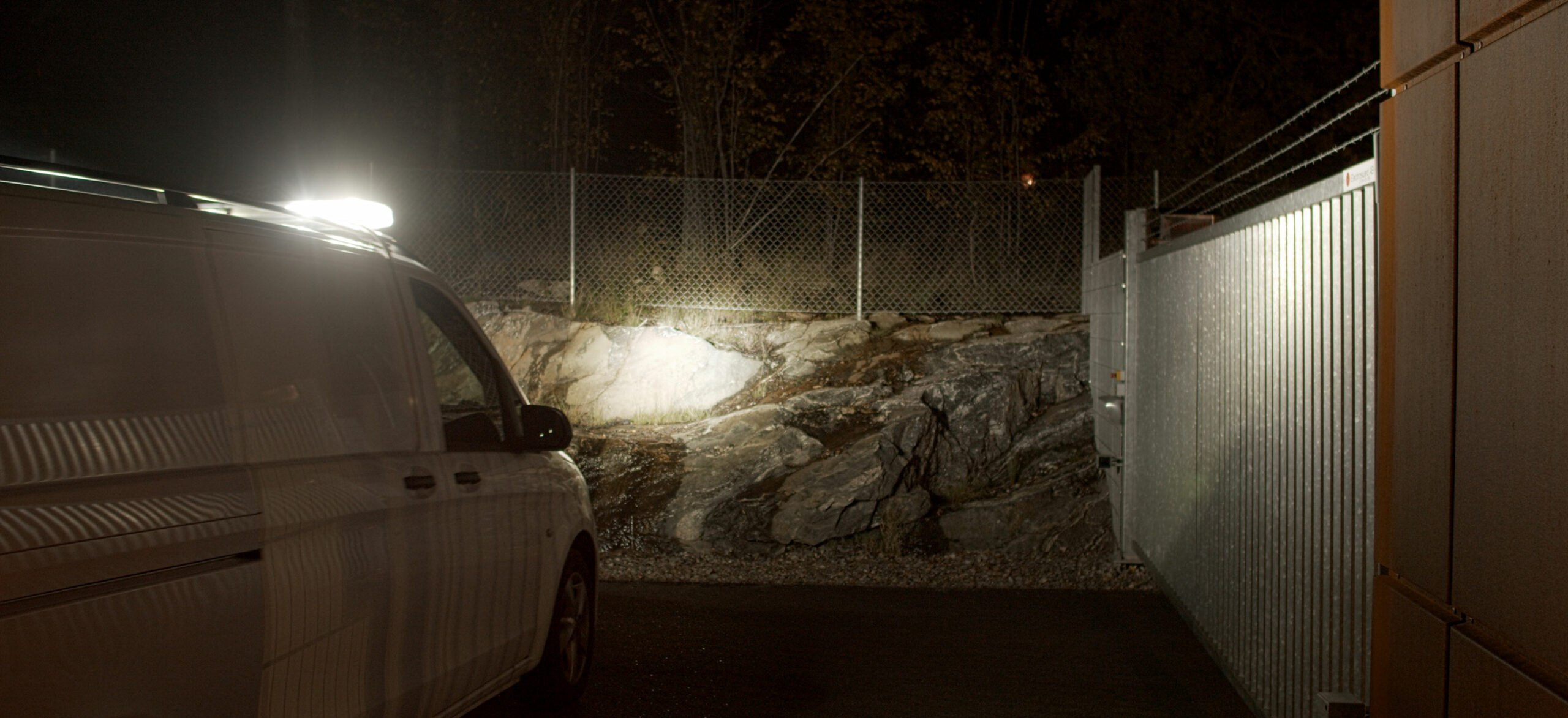 Bevakningsfordon med vitt ljus lyser upp en industriport.