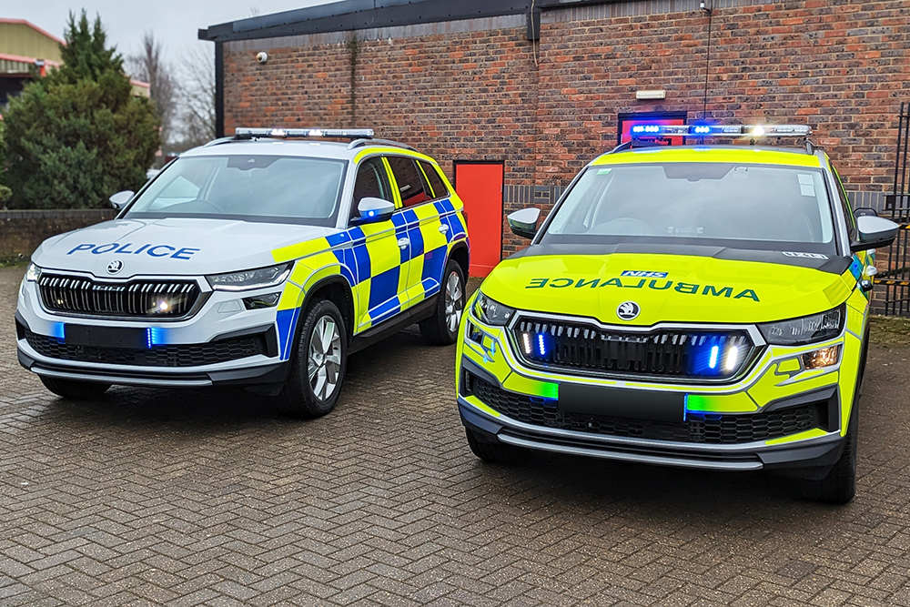 Police and Ambulance Skoda Kodiaqs with Hazard Warning Lighting in front of Brick Building