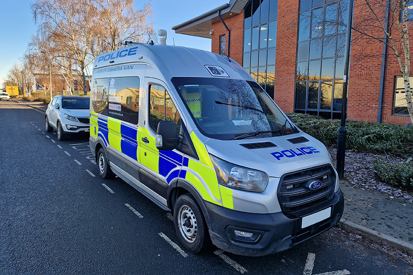 Angle View of Police Safety Camera Van Parked on Road Outside Office Type Building in Front of White Car