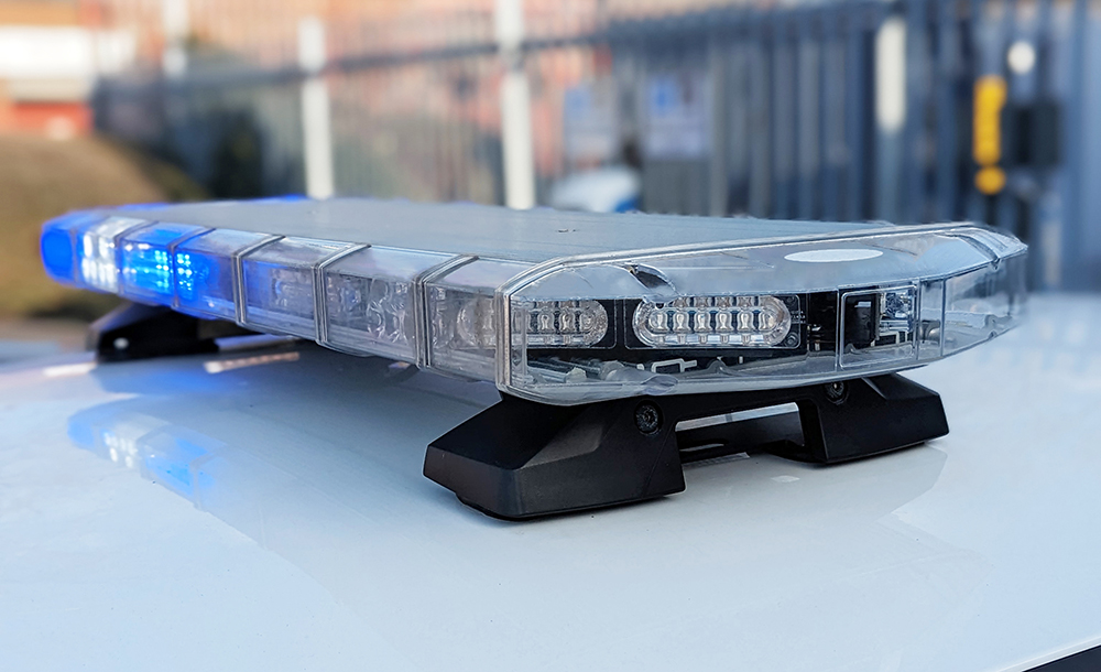 Closely Cropped Angle View of the Blue and White Stellar Lightbar on Top of a White Vehicle Roof, Railings in the Background are Out of Focus