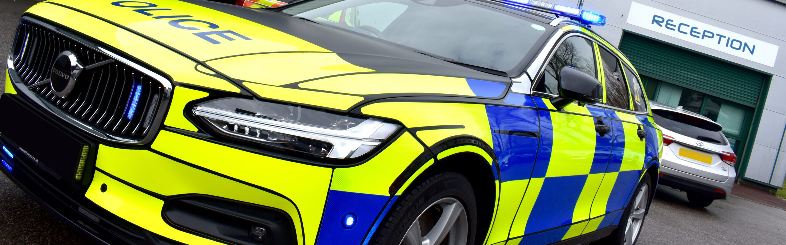 Close up angle view of police car in front of a grey garage building with a Reception sign above the entrance