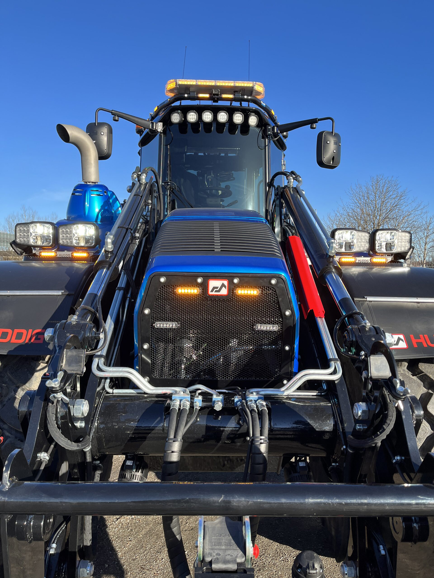 Front view of Blue Excavator with Various Amber LED Modules and Amber W3 Lightbar with Blue Sky in Background