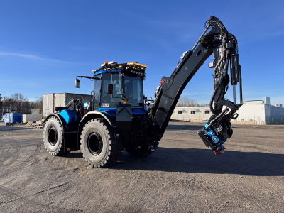 Angle View of Blue Excavator with Various Amber LED Modules and Amber W3 Lightbar with Blue Sky and Grey Industrial Building in Background