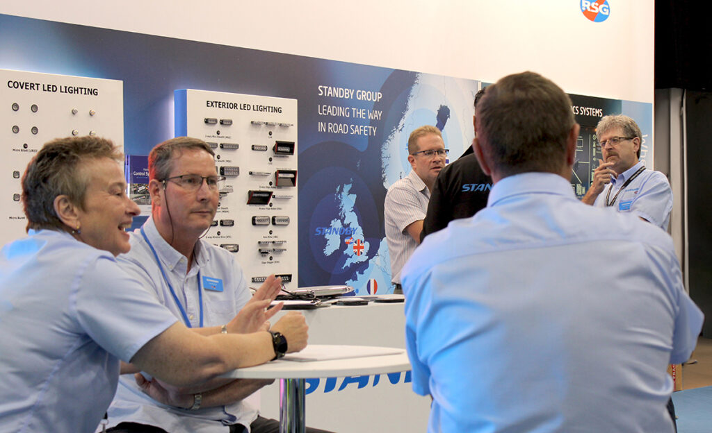 Over shoulder view of staff on Standby's NAPFM stand, group in conversation at table and group in distance
