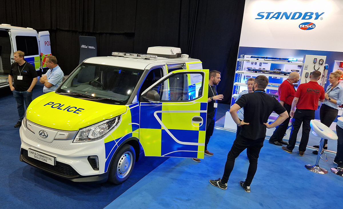 NAPFM Standby Stand Police Van, various groups of people stand around it talking, the passenger side door opens onto the stand