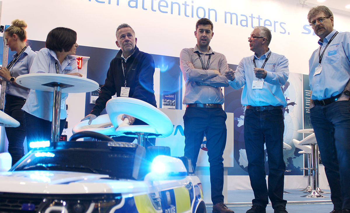 Shot taken from ground level looking up at people stood behind children's ride-on RC car with blue flashing lights, which is cropped and slightly out of focus at the bottom of the image