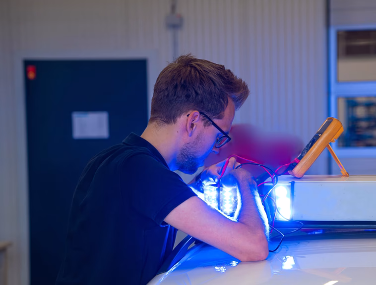 Employee working on a lightbar with multimeter in situ on top of a vehcile.