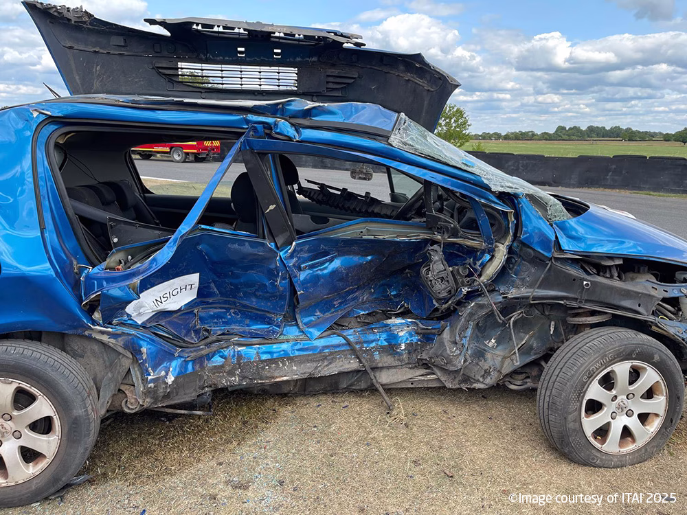 Side on view of a dark blue car at ITAI Crash Day 2025. Both driver side doors are concave where an impact has taken place.