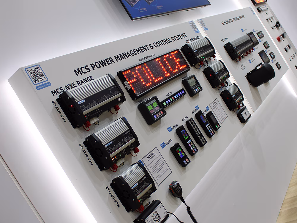 Angle view of MCS Power Management & Control Systems and Specialised Vehicle System white panels mounted on a white wall with various Standby UK control products and a Traffic Commander Matrix Sign which reads 'Police'.