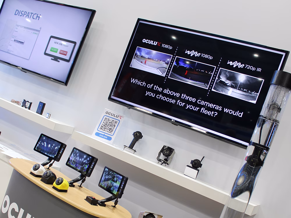 Angle view of the Oculux camera area on the Standby UK exhibition stand with a screen showing a presentation on the Oculux, with cameras and screens in front. A tube of water houses 2 cameras, one is under water and one above. The Fleetmotus range can also be seen on the lefthand side.