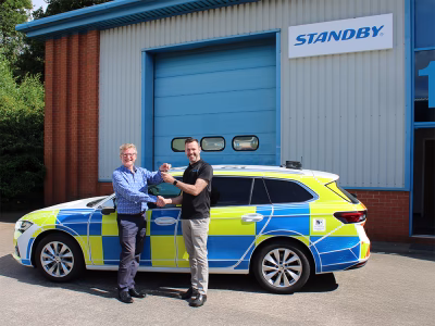 Roy McClarty and Robert Blakemore shake hands in front of a police car outside of the Standby building, Robert handing the keys over to Roy.