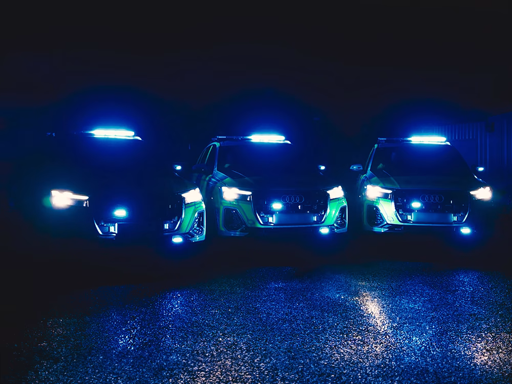 Three Police cars at night parked in a row each with identical blue lights illuninated on a wet carpark